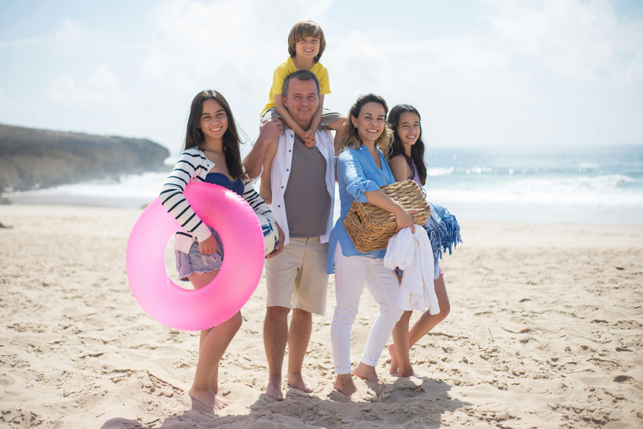 A family of a mom, dad, two teenage daughters, and a young son poses on a sunny beach